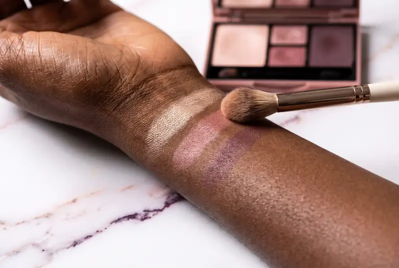 Eyeshadow swatches in champagne, rose and plum on a forearm, with a blending brush