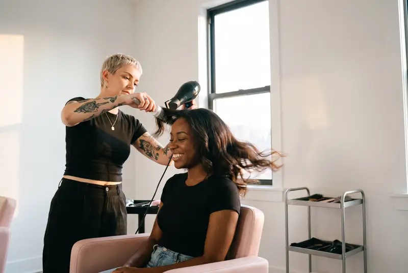 A hair stylist blow-dries glossy waves as her client smiles