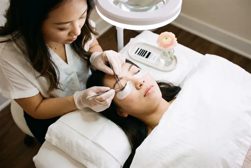 A lash artist places an extension while her client rests under a ring light
